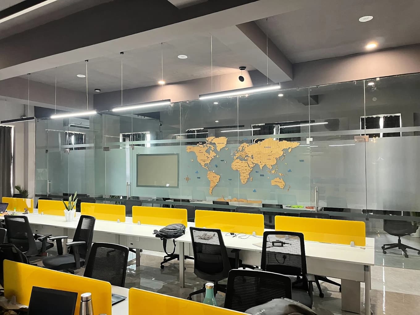 Coworking benches with yellow dividers in front of glass-walled rooms decorated with a wooden world map