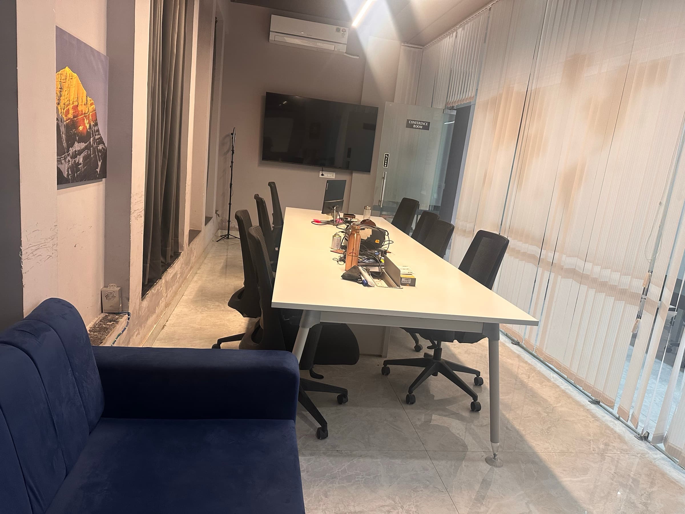 Conference room with a long white table, mesh chairs, wall-mounted screen and a navy sofa for guests