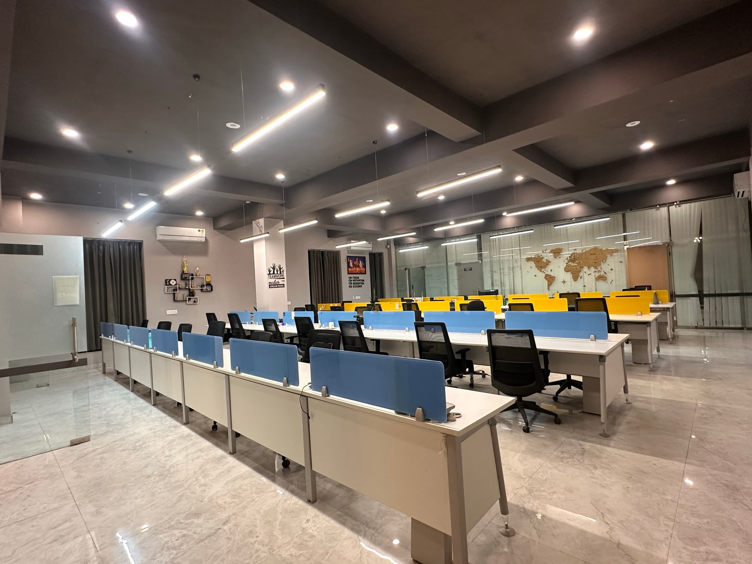 Wide view of the JaipurCowork open-plan floor with rows of white workstations, blue and yellow desk dividers and linear ceiling lights