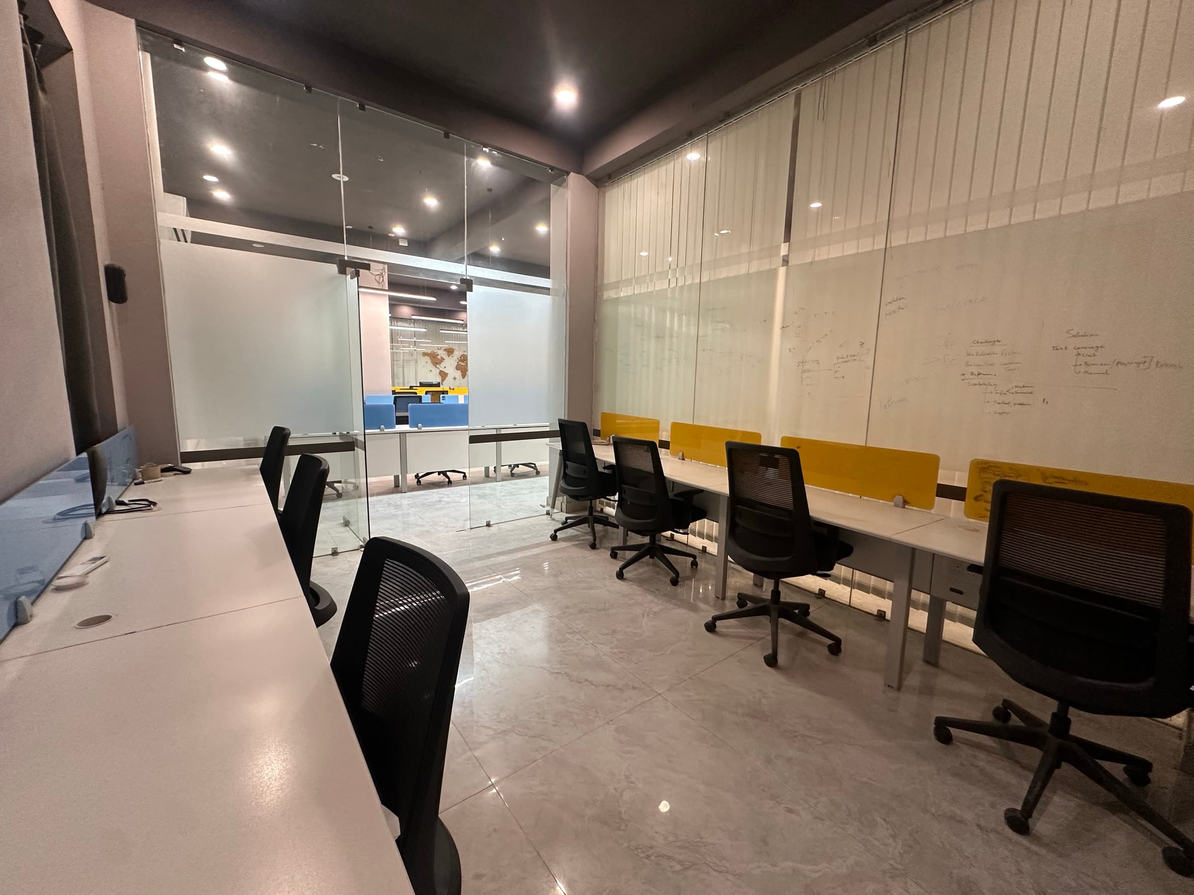 Glass-walled team cabin with workstations along both sides and planning notes written on the glass
